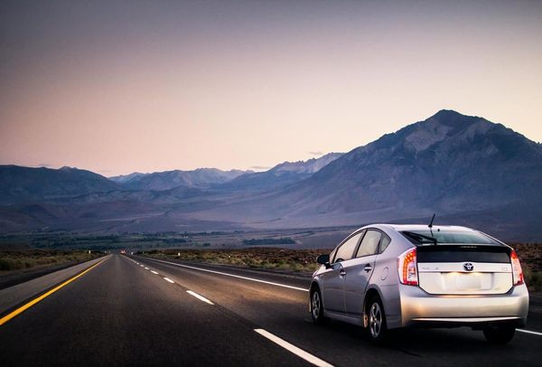 A silver Toyota Prius driving on an open road toward a mountain range at dusk.